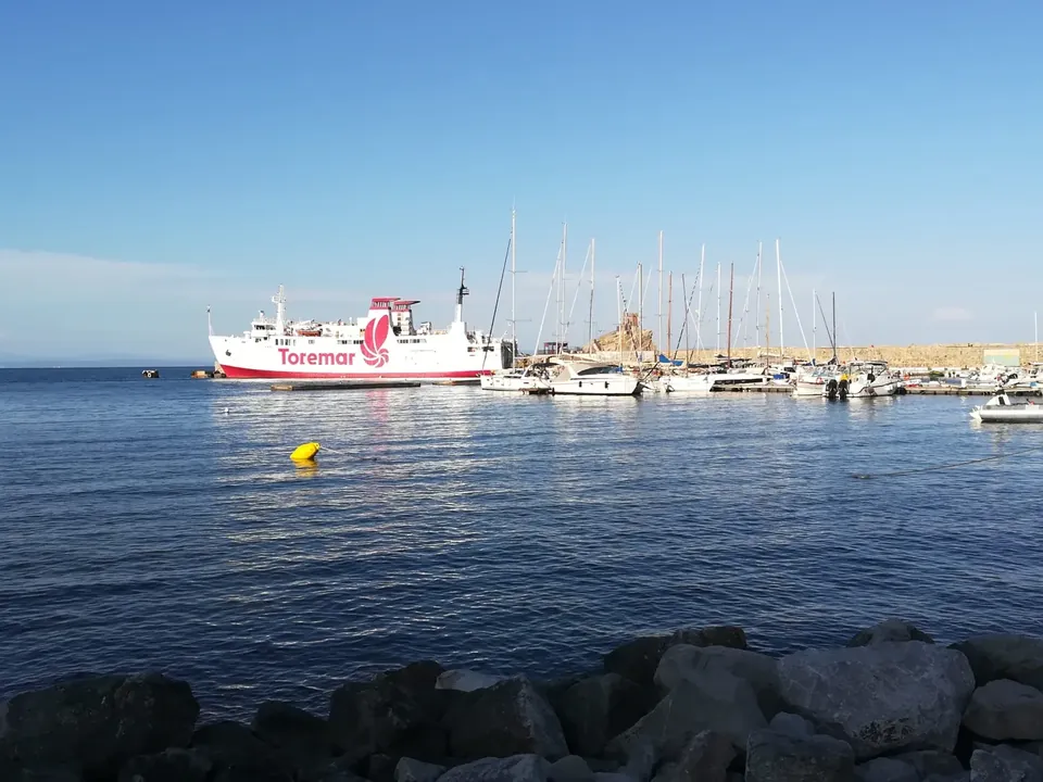 Ferri de Toremar en el puerto junto a veleros y un muelle de piedra