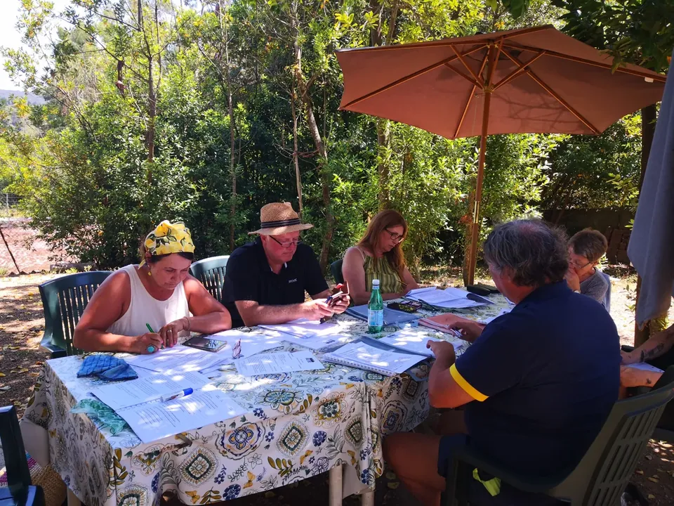 Adultos trabajando con su profesora y los materiales del curso a la sombra de los árboles de Villa Teresa