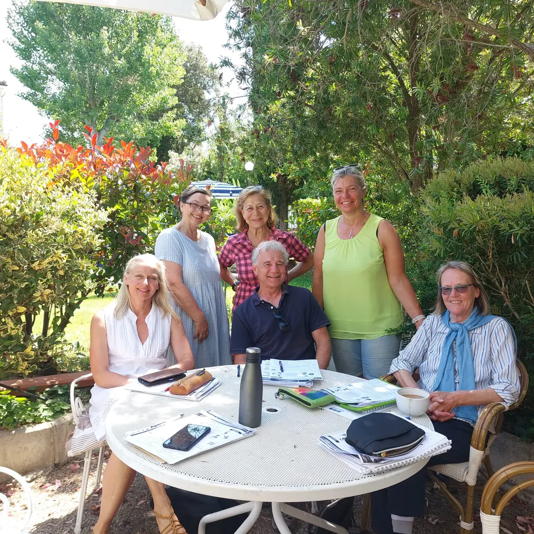Sechs Personen an einem Tisch im Garten mit Tafel und Lernmaterialien